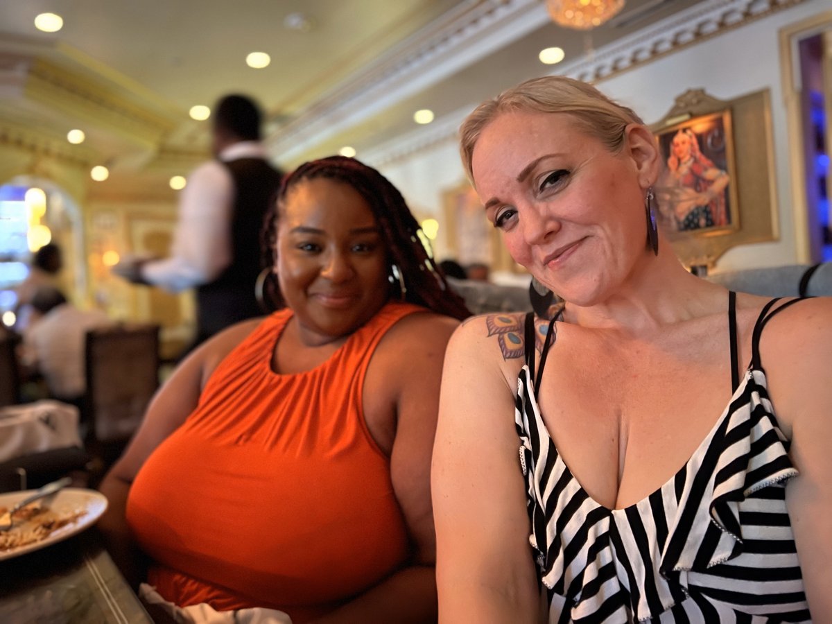 Kernika and Dana sitting at dinner table at Royal Taj restaurant in MD; Kernika is wearing orange sun dress, Dana is wearing black and white striped sun dress.